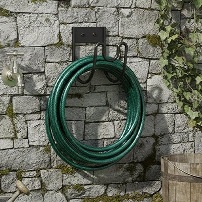 Support tuyau arrosage accroché sur le mur d’un jardin avec un tuyau bien arrangé