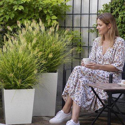 une femme assise dons son jardin décore avec des pot de Plante artificielle en forme herbe à roseaux