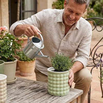 un homme arrose une plante dans le mini Pot de fleur qui décore sa terrasse 